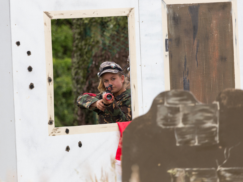 Girl dressed in camoflage behind a prop of a building playing laser comabt
