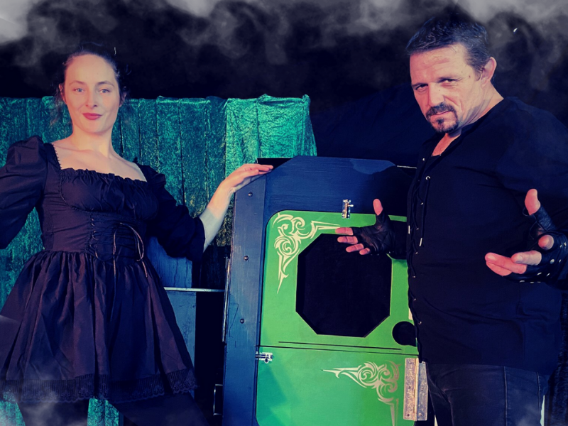 Magician and his assistant dressed in black with a magic box behind them ready to perform at a family attraction in the midlands